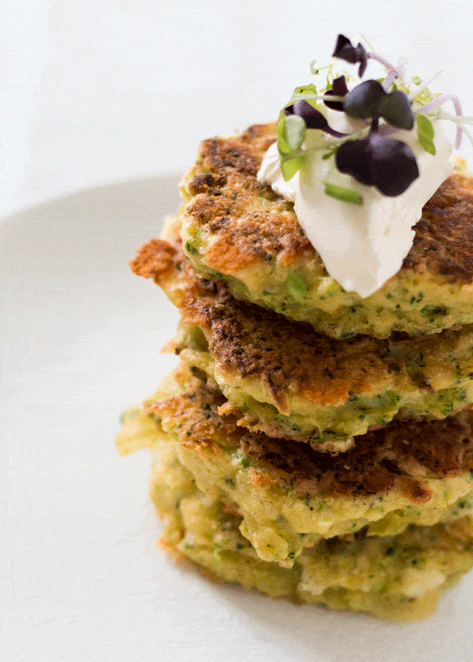 Cheddar Broccoli Fritters served on a white plate with a dollop of sour cream and micro greens