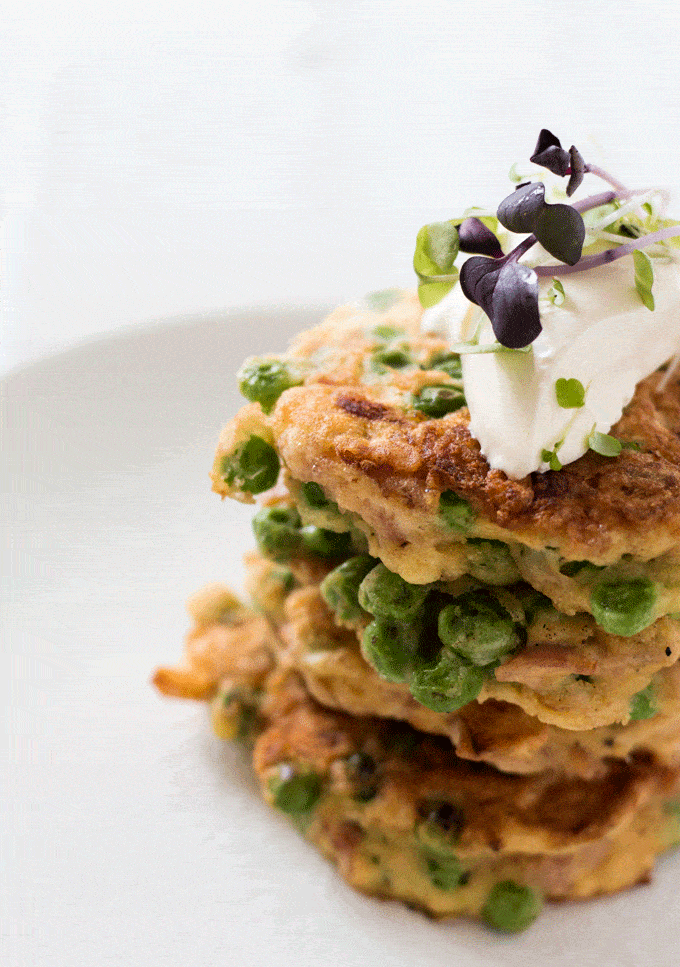 A stack of ham and pea fritters on a white plate topped with sour cream and microgreens