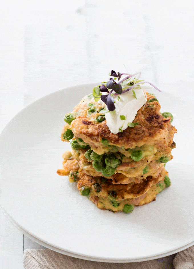 Stack of Ham and Pea Fritters on a white plate topped with sour cream and micro greens 