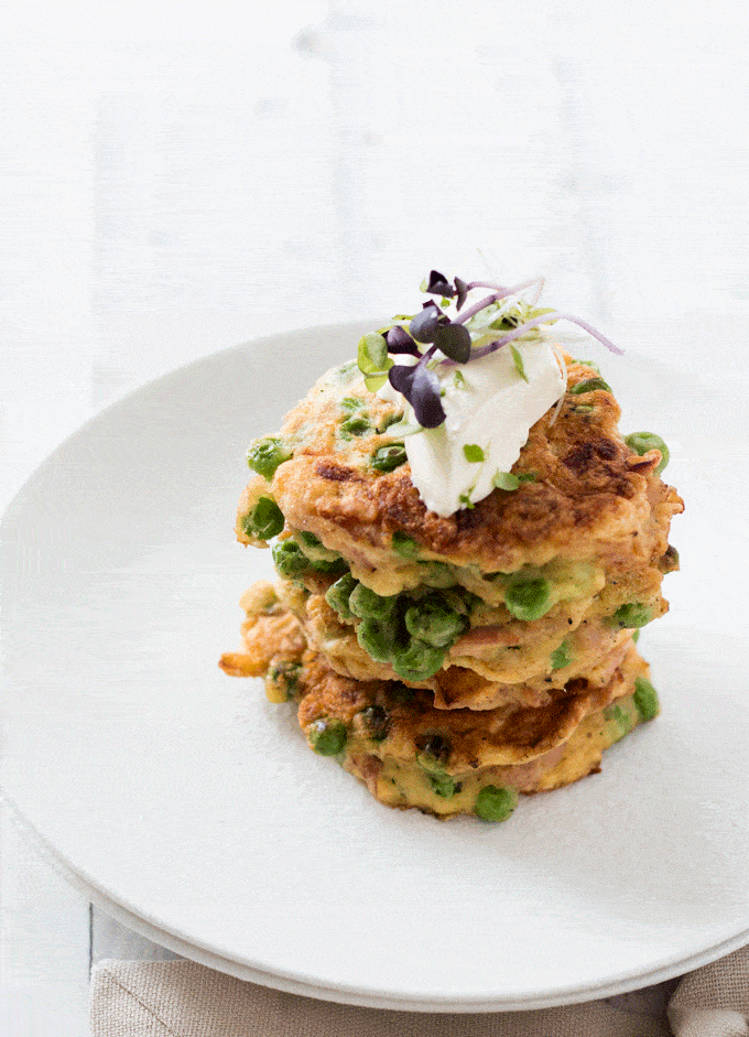 Stack of Ham and Pea Fritters on a white plate topped with sour cream and micro greens