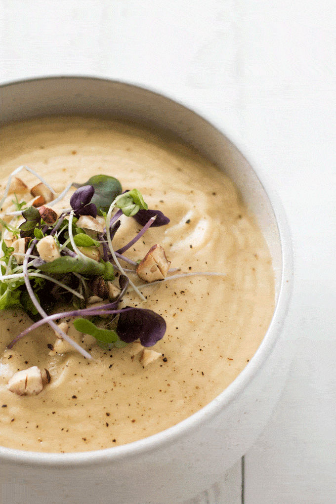 close up shot of Cauliflower and Parsnip Soup served in an off white bowl and topped with toasted hazelnuts and microgreens