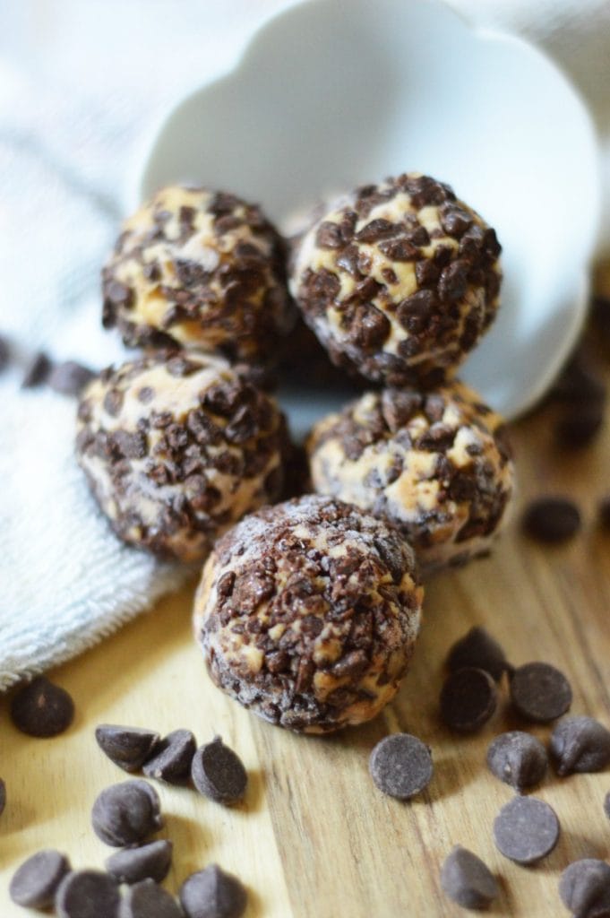 close up of chocolate cheesecake fat bombs on a wooden background surrounded by chocolate chips