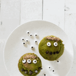 two green monster muffins on a white plate surrounded by candy eyes
