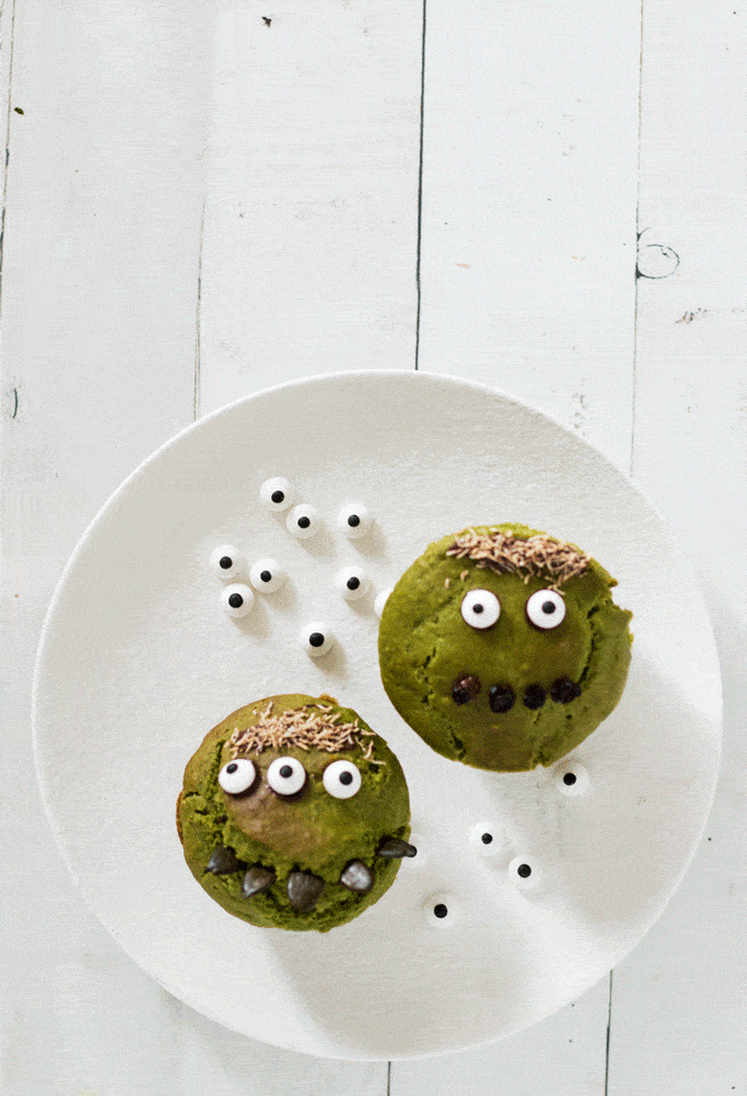 two green monster muffins on a white plate surrounded by candy eyes
