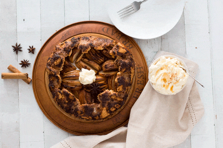 warm apple crostata on a wooden board surrounded by fresh cream, star anise and cinnamon