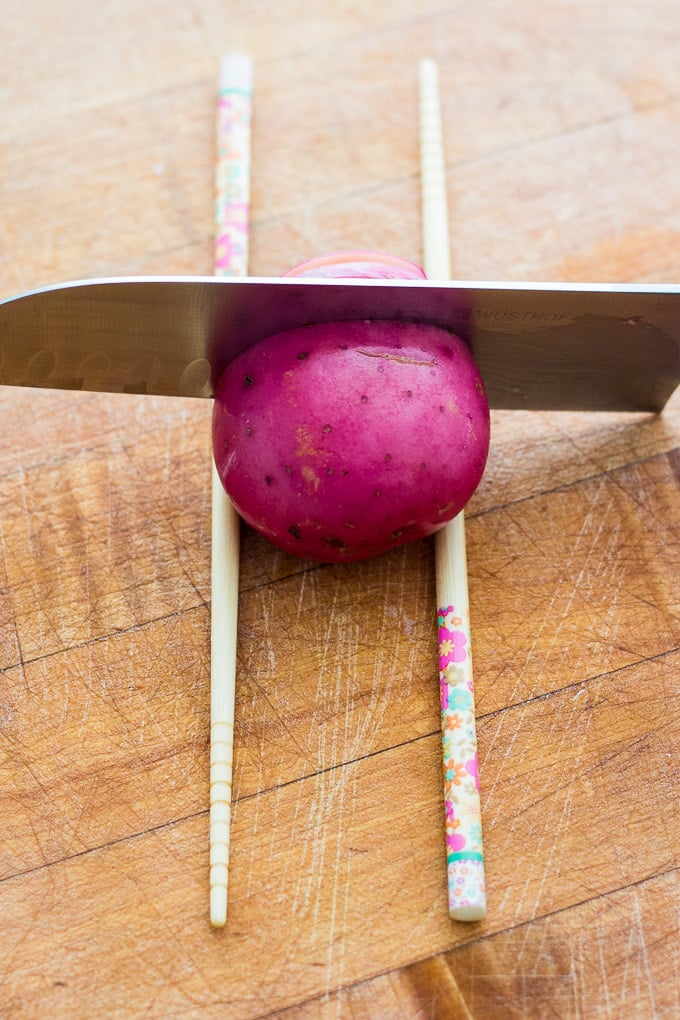 using two chopsticks to chop the veggies and garlic hasselback potatoes