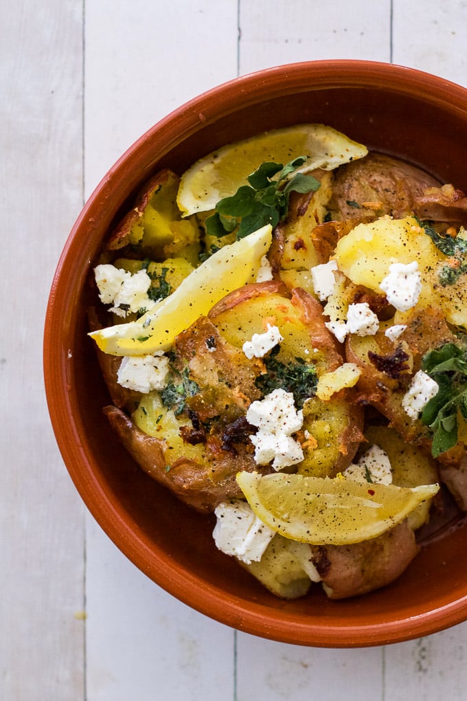 lemon garlic potatoes in a terracotta bowl with lemon wedges and feta on top