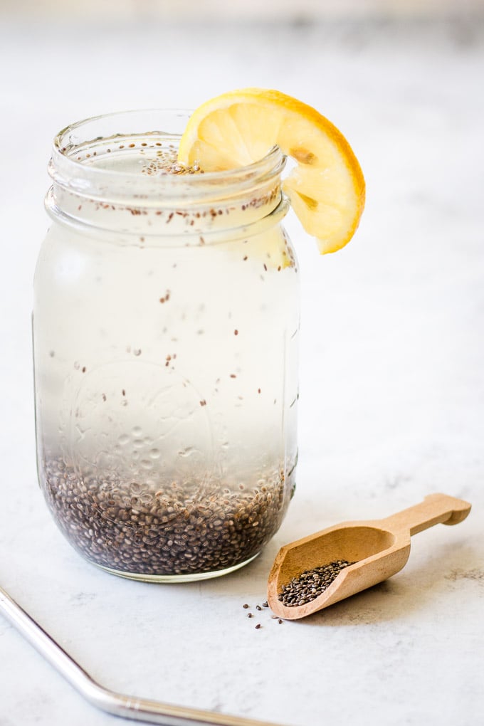 a tall glass of water with chia seeds in the bottom and a slice of lemon on the side