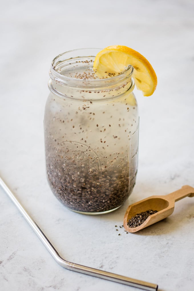top view of chia water in a glass with chia seeds floating on top, a slice of lemon, and a small spoon full of seeds on the side