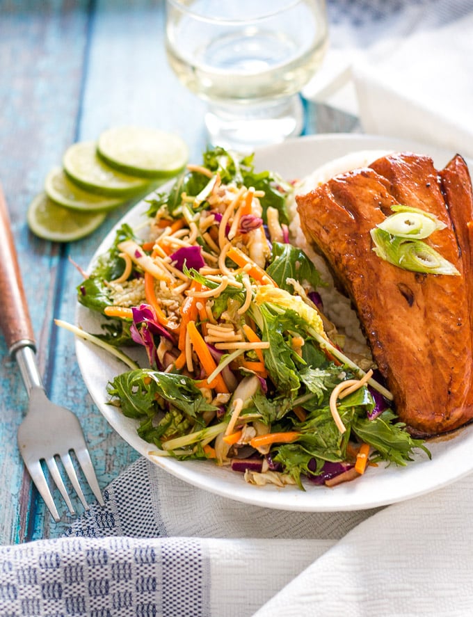 teriyaki glazed salmon served with a side of asian slaw with some lime slices in the background