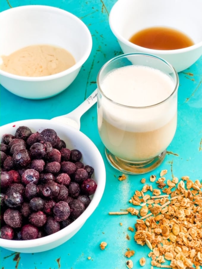 ingredients for making a blueberry almond milk smoothie laid out on a teal background