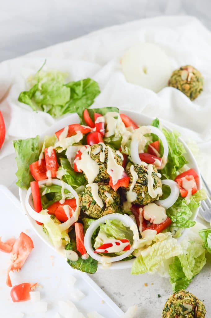 Falafel salad in a white bowl: homemade falafel, lettuce, onion, bell pepper and a creamy dressing