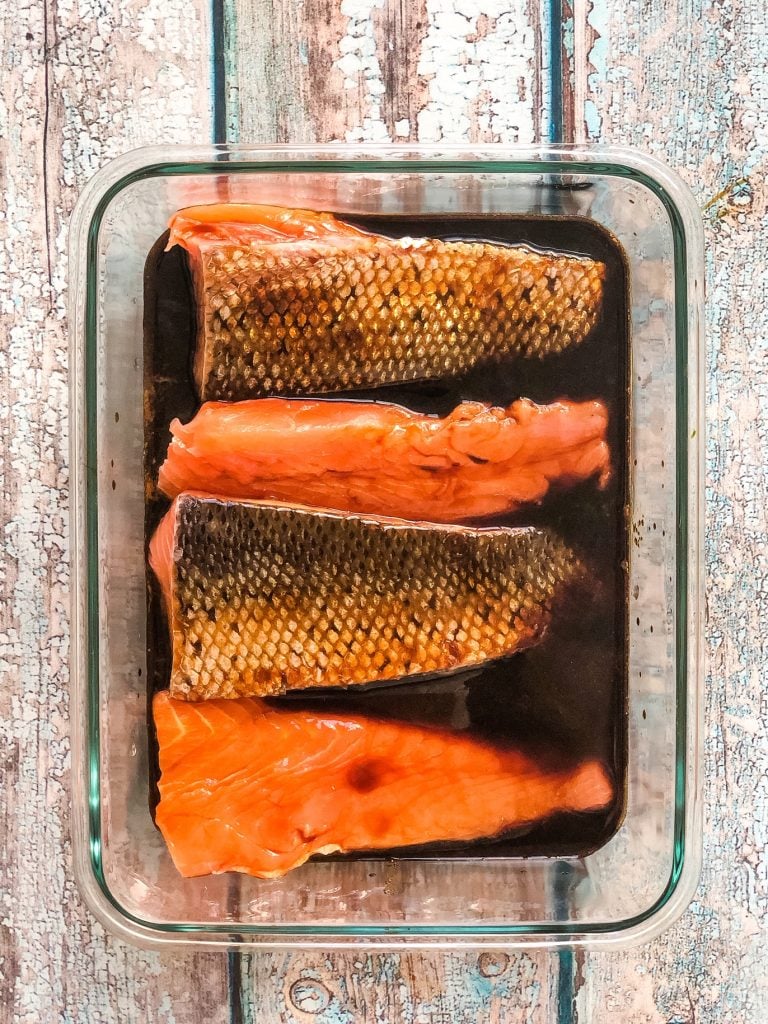 4 salmon fillets in a glass container marinading in a teriyaki glaze