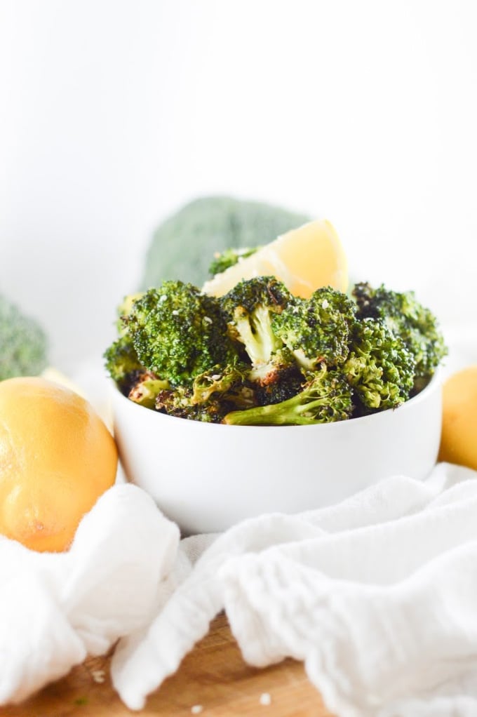 Air fryer broccoli in a white bowl with fresh lemon wedges on top