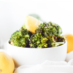 Air fryer broccoli in a white bowl with fresh lemon wedges on top