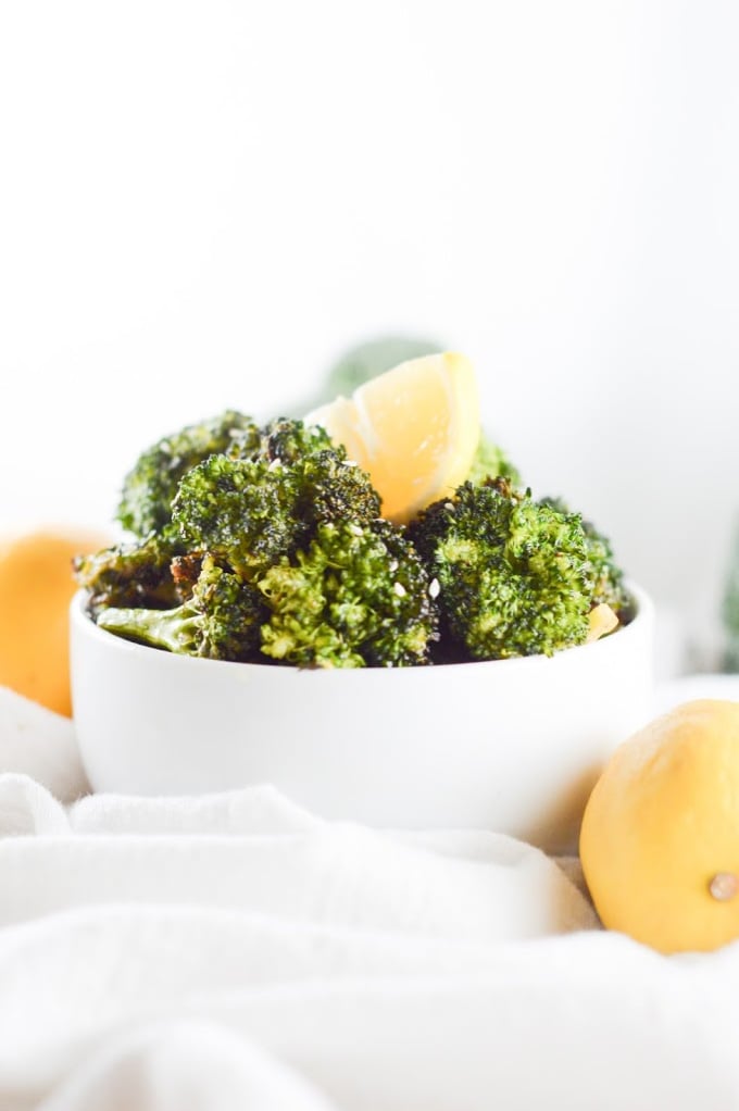 Air fryer broccoli piled in a white bowl with fresh lemon wedges