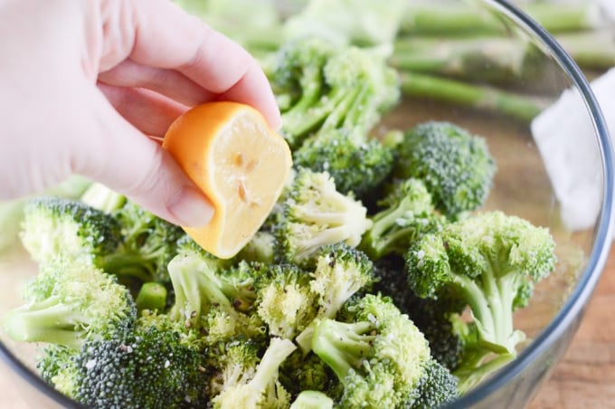 Broccoli florets in a bowl and lemon being squeezed over