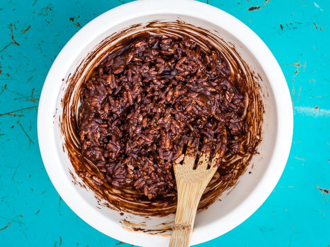 white bowl containing chocolate and rice bubbles being stirred by a wooden spoon