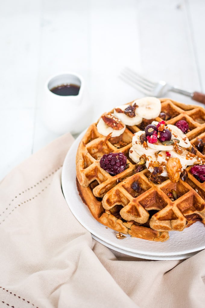 oat flour waffles on a white plate topped with banana slices and berries