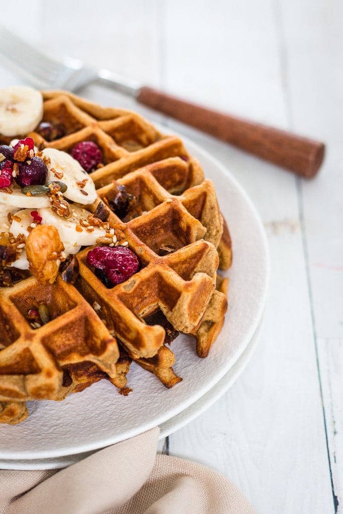 close up shot of banana waffles on a white plate topped with banana slices and berries