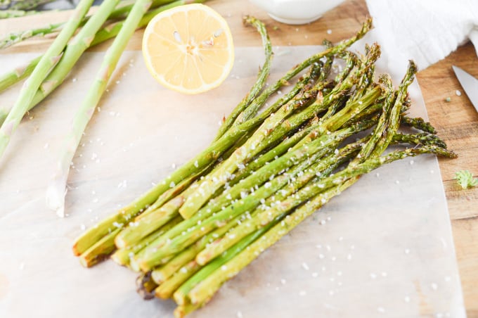 Air fryer asparagus on a wooden board with lemons in the background