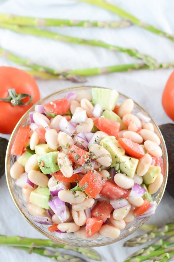Avocado white bean salad in a glass bowl surrounded by fresh veggies