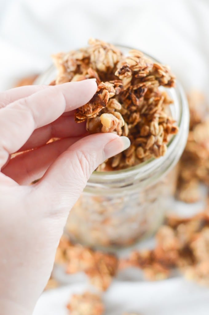 Hand picking up a cluster of homemade granola from a glass jar