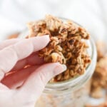 Banana bread granola being lifted in clusters from a glass mason jar