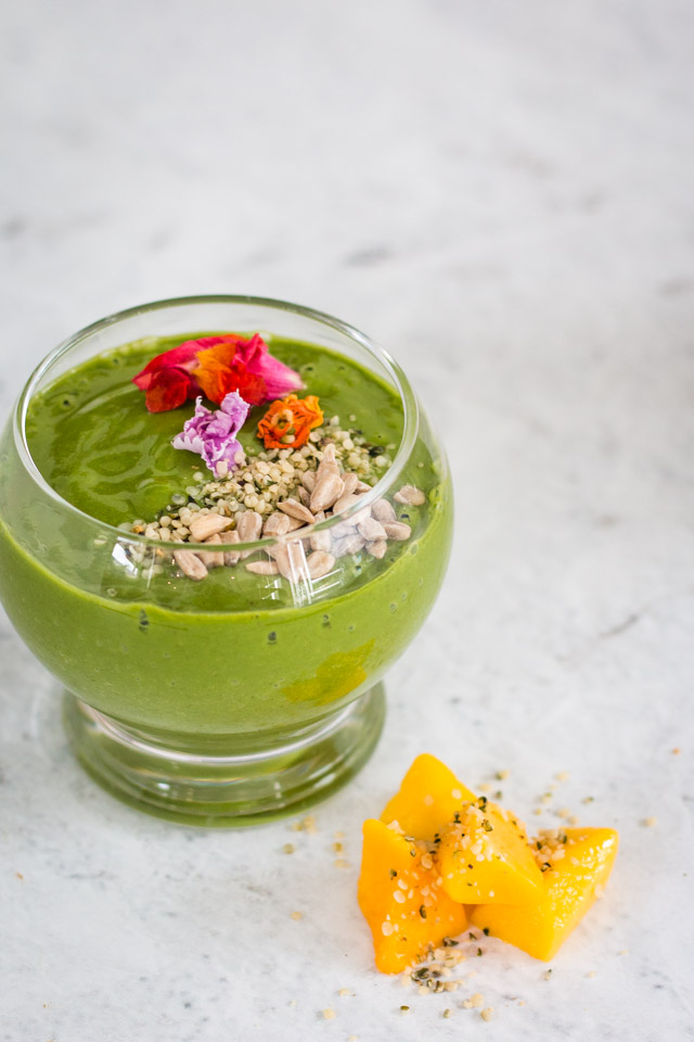 green smoothie served in a small glass and topped with hemp seeds, sunflower seeds and edible flowers