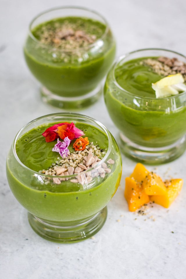 Three green smoothies served with edible flowers on top