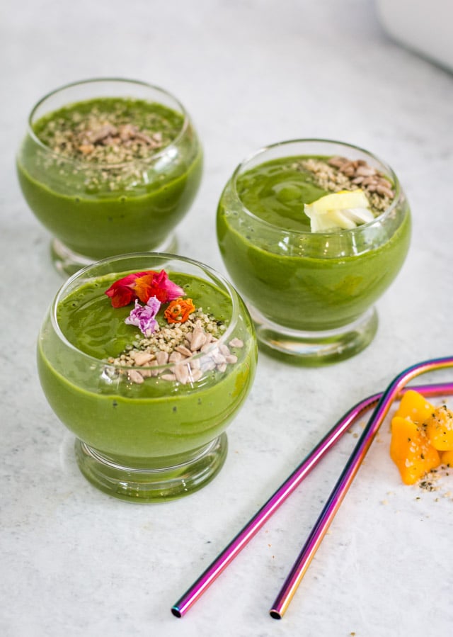 3 Mango banana spinach smoothie s in glasses topped with edible flowers and seeds