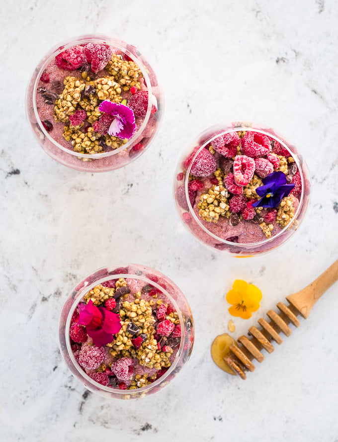 Raspberry chia pudding decorated with edible flowers, buckinis and cacao nibs