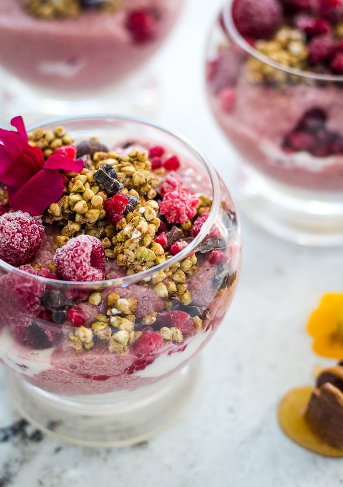 Raspberry chia pudding decorated with edible flowers, buckinis and cacao nibs