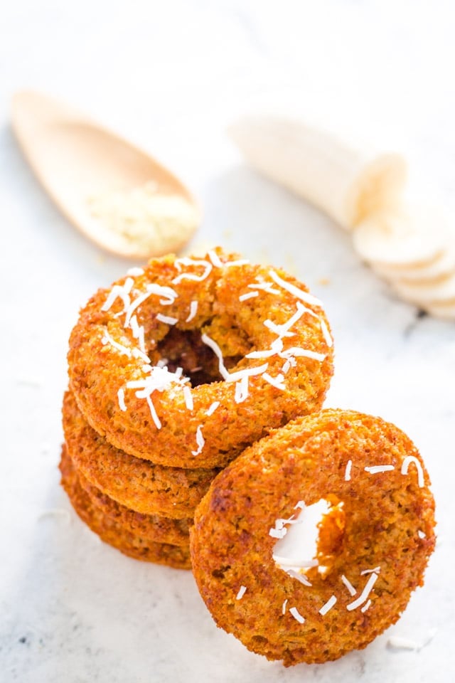 stack of banana donuts with a sprinkle of coconut on top and a spoonful of raw oats in the background