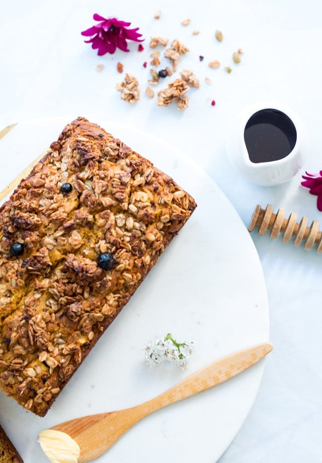 Healthy Pumpkin Bread on a white background surrounded by honey, honey spreader and some granola