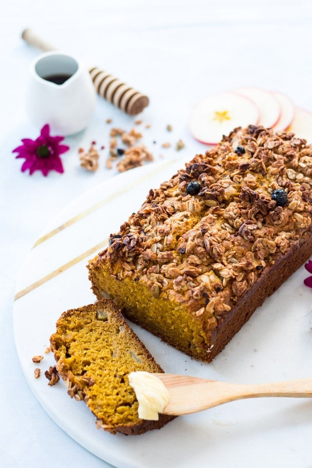 Pumpkin Bread and Apple and Granola sliced and some butter being spread on with a wooden utensil