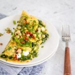 Cabbage omelette on a white plate topped with fresh chilli and sprouts