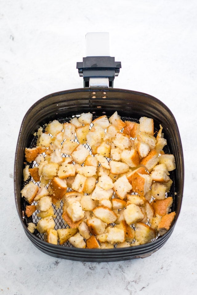 air fryer basket filled with an even layer of bread chunks soaked in olive oil, salt, pepper, garlic and parsley powder