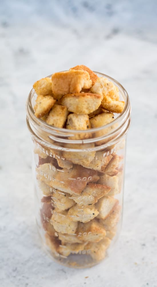 tall glass mason jar filled to overflowing with croutons against a grey background