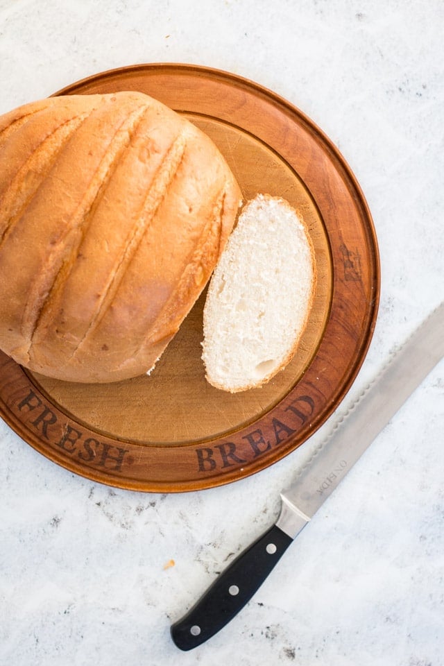 wooden chopping board with a big cob of bread on top and a bread knife beside it