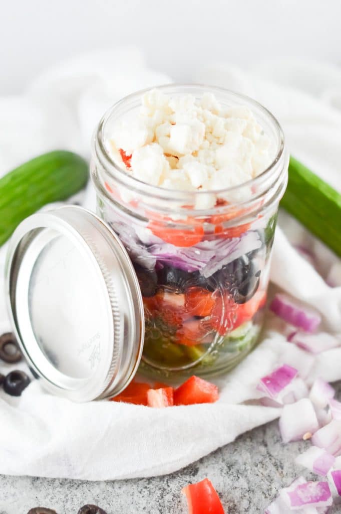 glass mason jar with greek salad ingredients layered inside