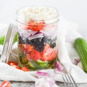 glass mason jars with greek salad ingredients layered inside