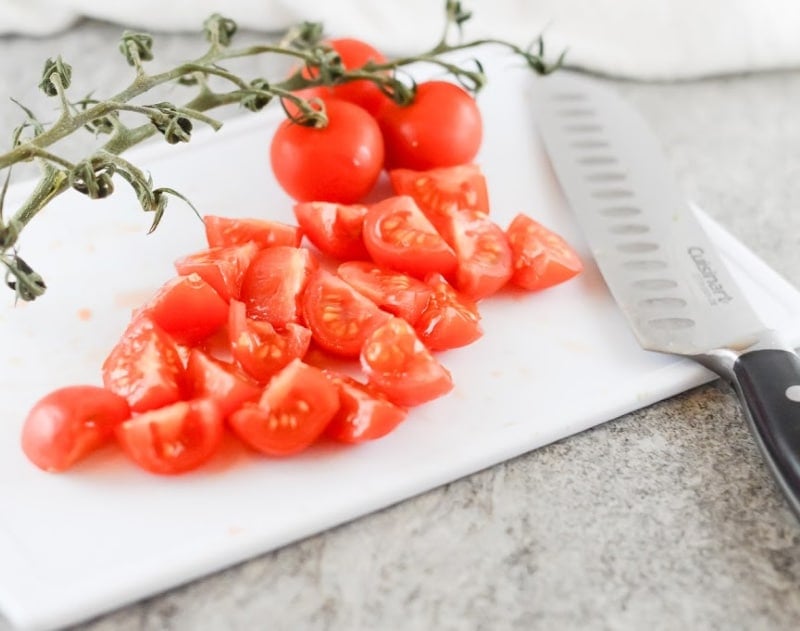 cherry tomatoes on a white chopping board cut into quarters