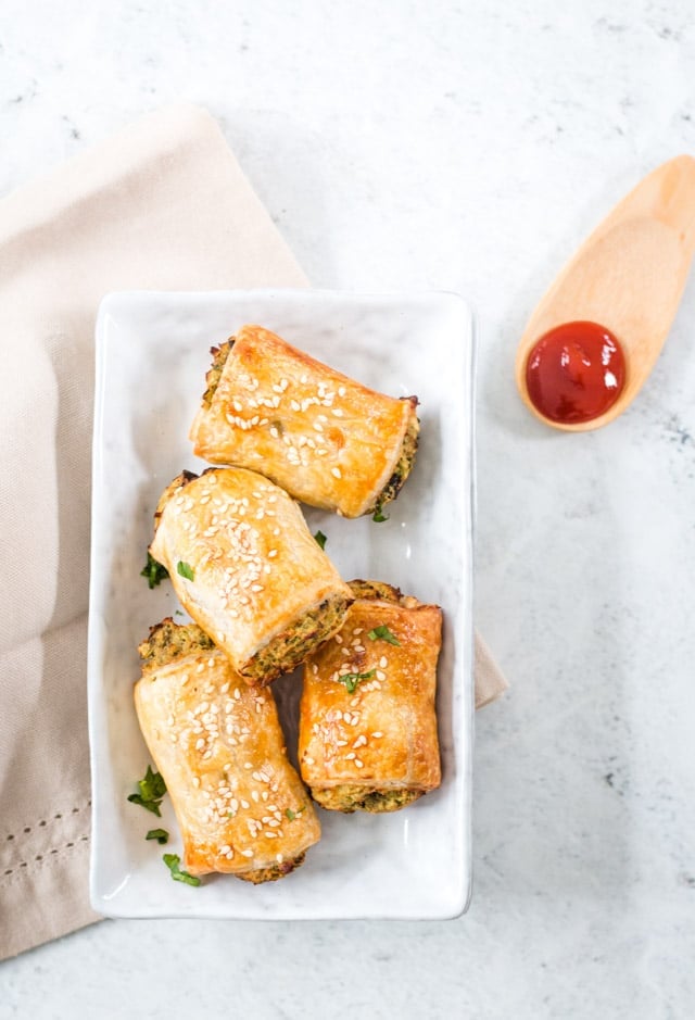 overhead shot of small sausage rolls on a white plate, small wooden spoon with a dollop of tomato ketchup