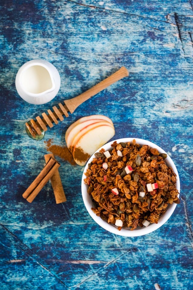 Overhead shot of apple cinnamon granola served in a white bowl against a dark blue background