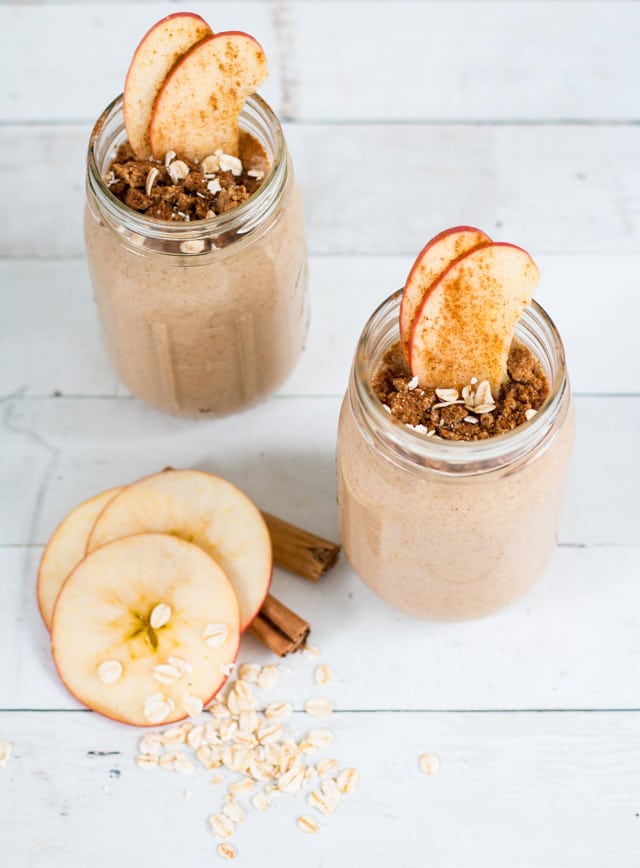 Two Apple Pie Smoothies in glass mason jars, topped with some thin apple slices and a sprinkle of cinnamon