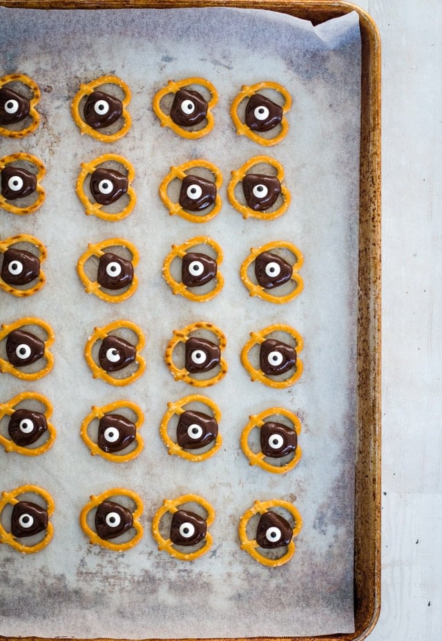 baking tray loaded with pretzels topped with chocolate and a google eye