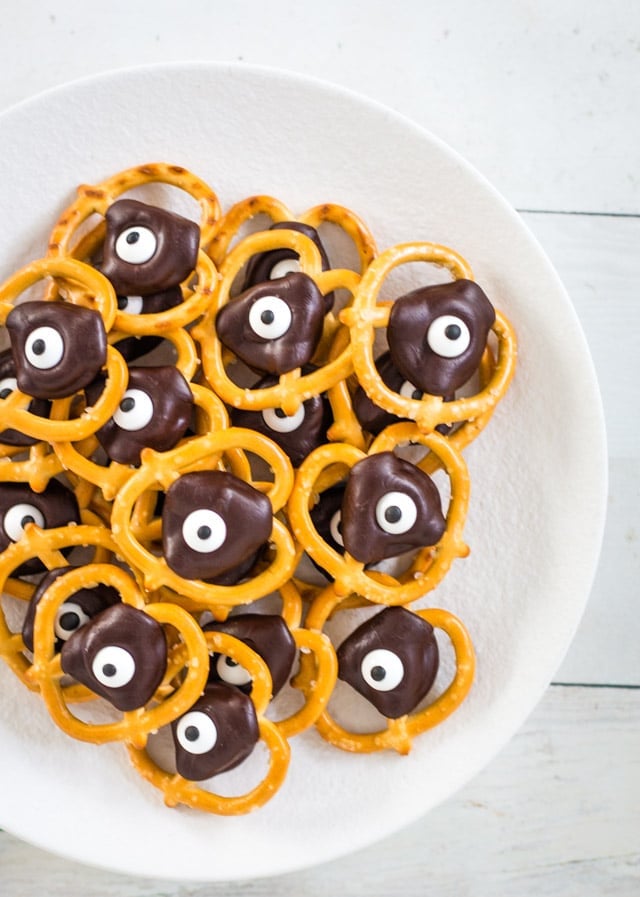 A white plate topped with a stack of halloween pretzels with google eyes and a chocolate topper