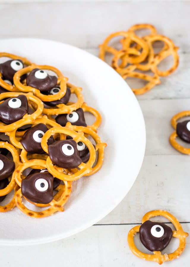 pretzels topped with chocolate and a googly eye on top of a white plate