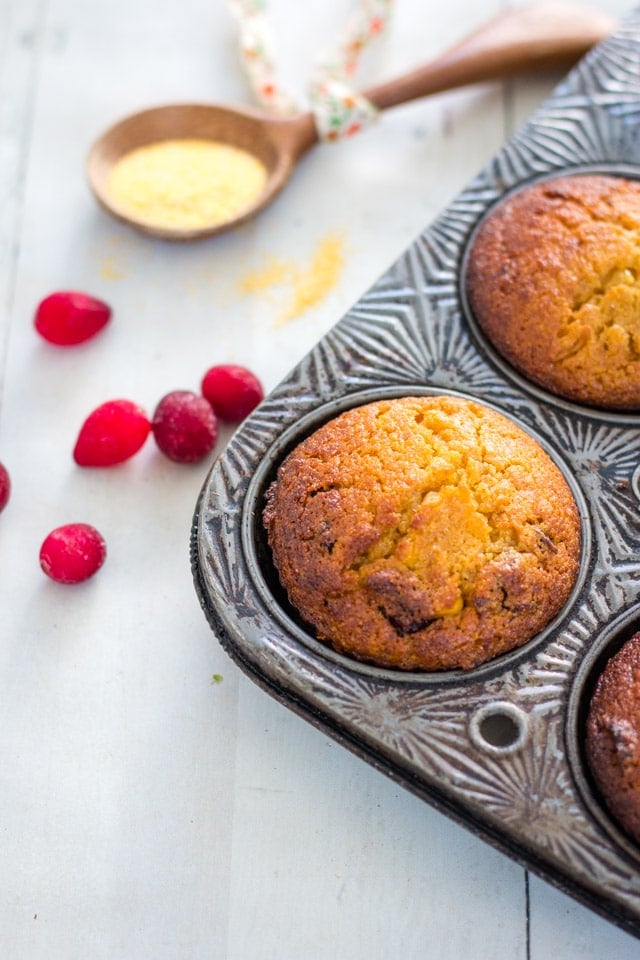 3 cranberry mini cornbread muffins in a vintage muffin tin on a white background